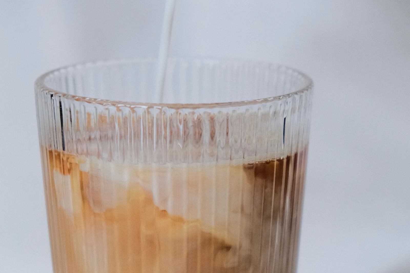 Milk being poured into an iced coffee in a ribbed glass